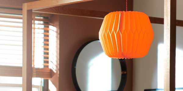 Image of an oval, orange paper shade hanging over a four poster bed.